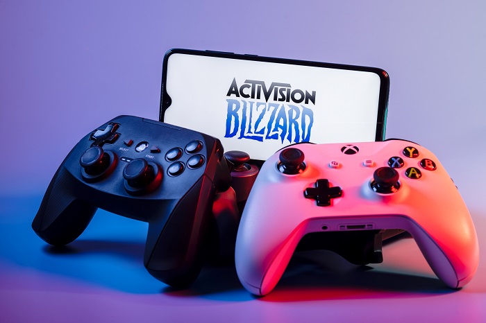 A smartphone with the Activision Blizzard logo on the screen on the pile of the gamepads.